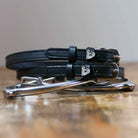 Black leather walrus spur straps with silver buckles angled on white wooden planks