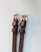 Black leather watermelon spur straps with silver buckles on a bright blue background