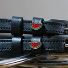 Close-up of enamel watermelon slice charms on black leather ManeJane spur strap keepers