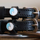 Close-up of round blue-and-white ocean wave charms on black leather spur straps