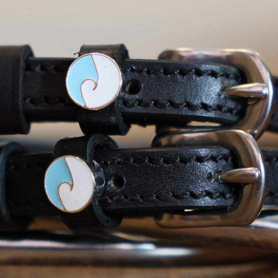Close-up of round blue-and-white ocean wave charms on black leather spur straps