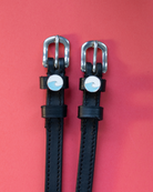 Black leather spur straps with round blue wave charms on a coral red background