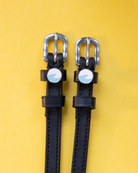 Blue wave charm spur straps in black leather flat-laid on a yellow background