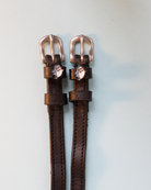 Black leather ManeJane spur straps with silver buckles and blue shark head charms on grey-blue