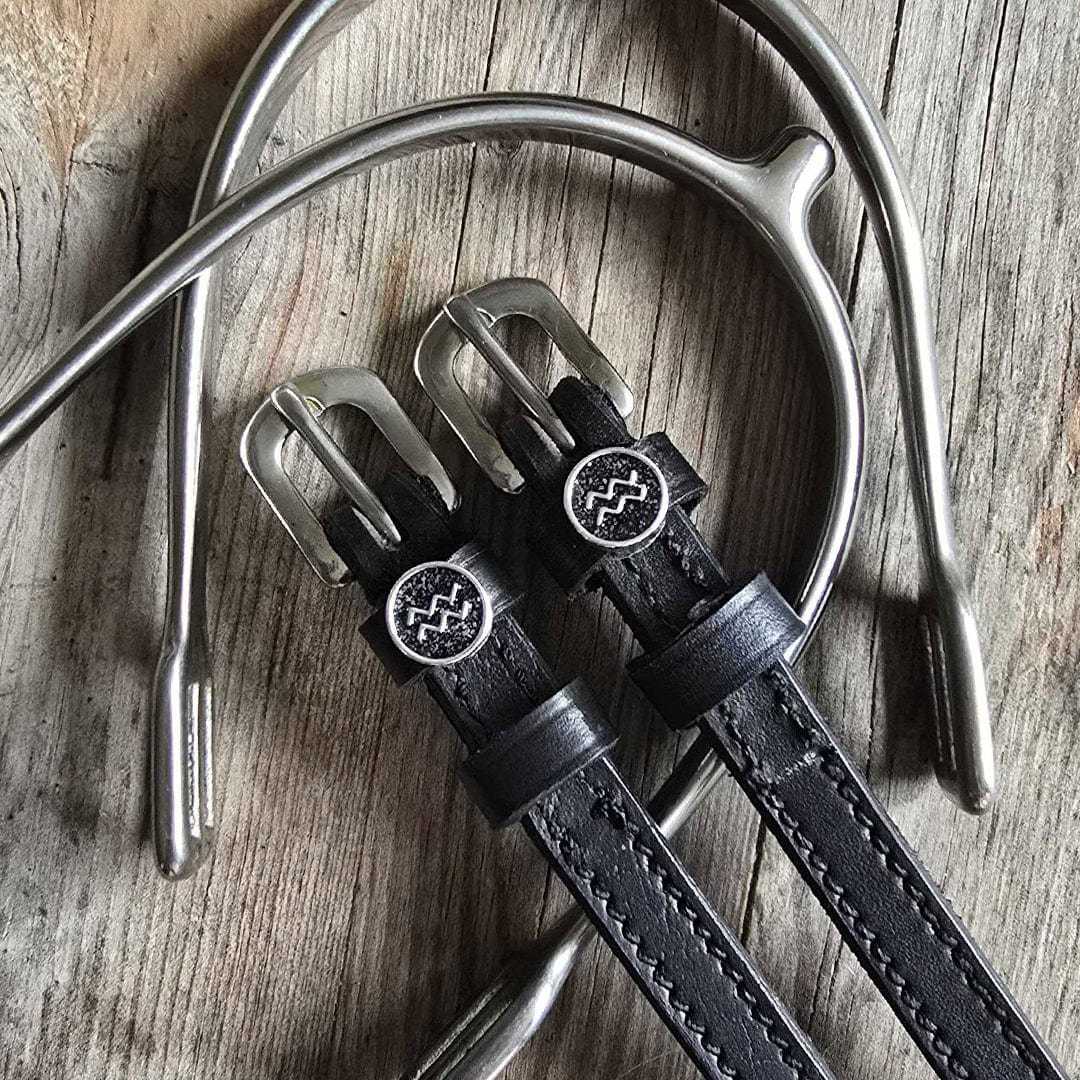 Black leather Aquarius Spur Straps with stainless steel buckles and custom charm on wooden background