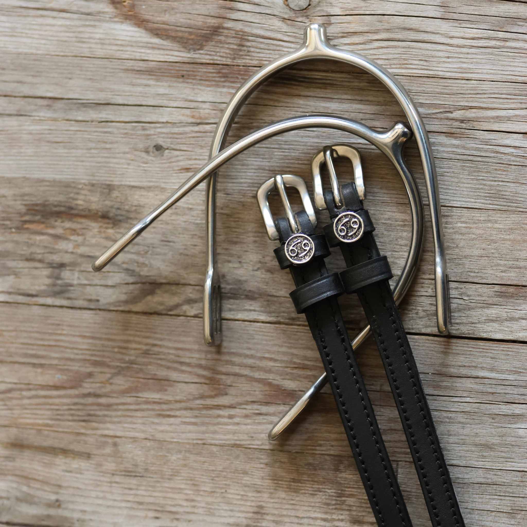 Black leather Cancer Spur Straps with stainless steel buckles and custom Cancer zodiac charms on wooden background