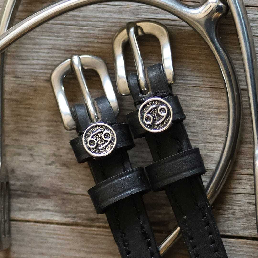 Black leather Cancer Spur Straps with stainless steel buckles and custom Cancer zodiac charms on wooden background