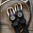 Black leather Cancer Spur Straps with stainless steel buckles and custom Cancer zodiac charms on wooden background