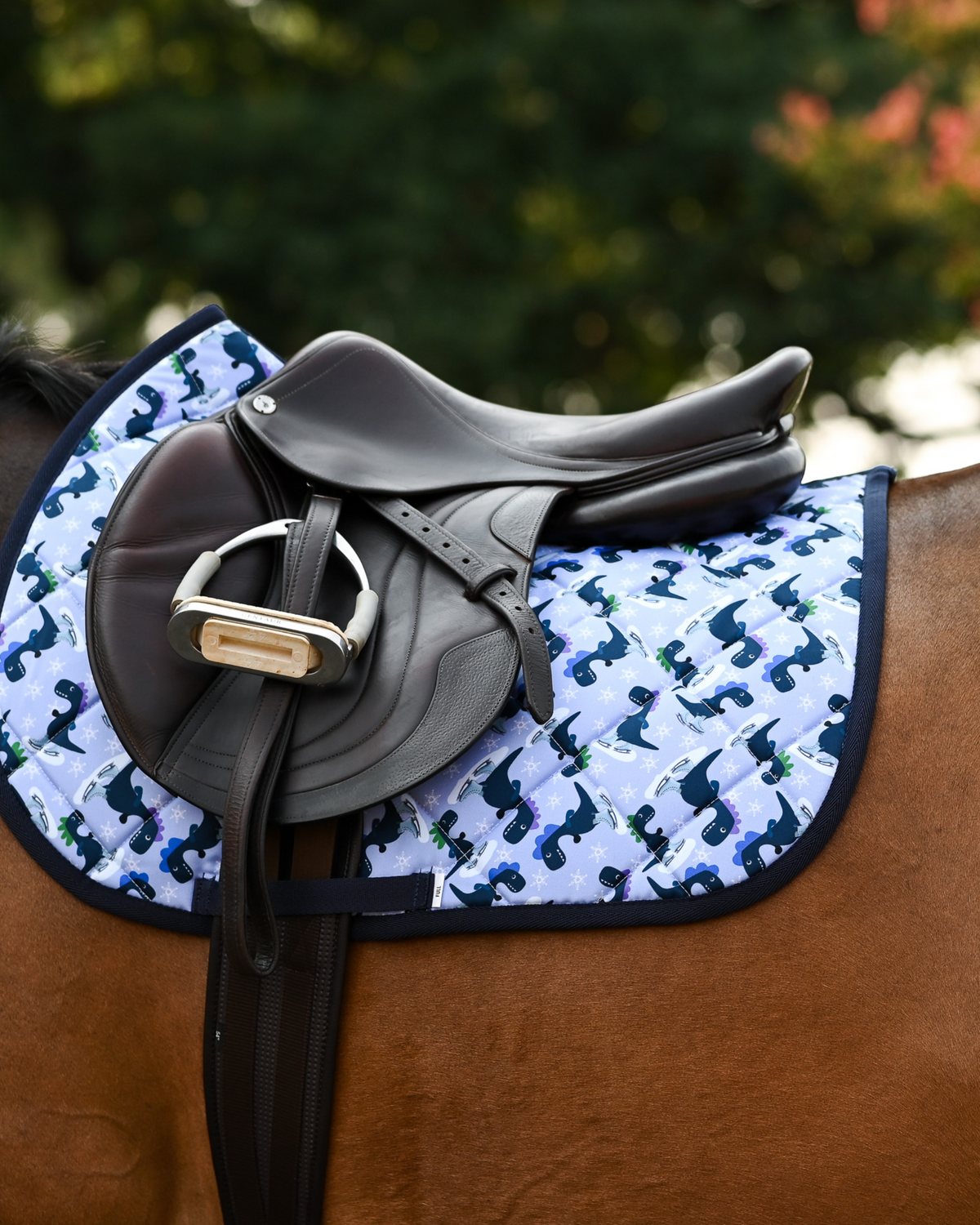 Periwinkle Dino-skate pad under a brown close-contact saddle, navy dinosaurs and snowflakes across the quilting
