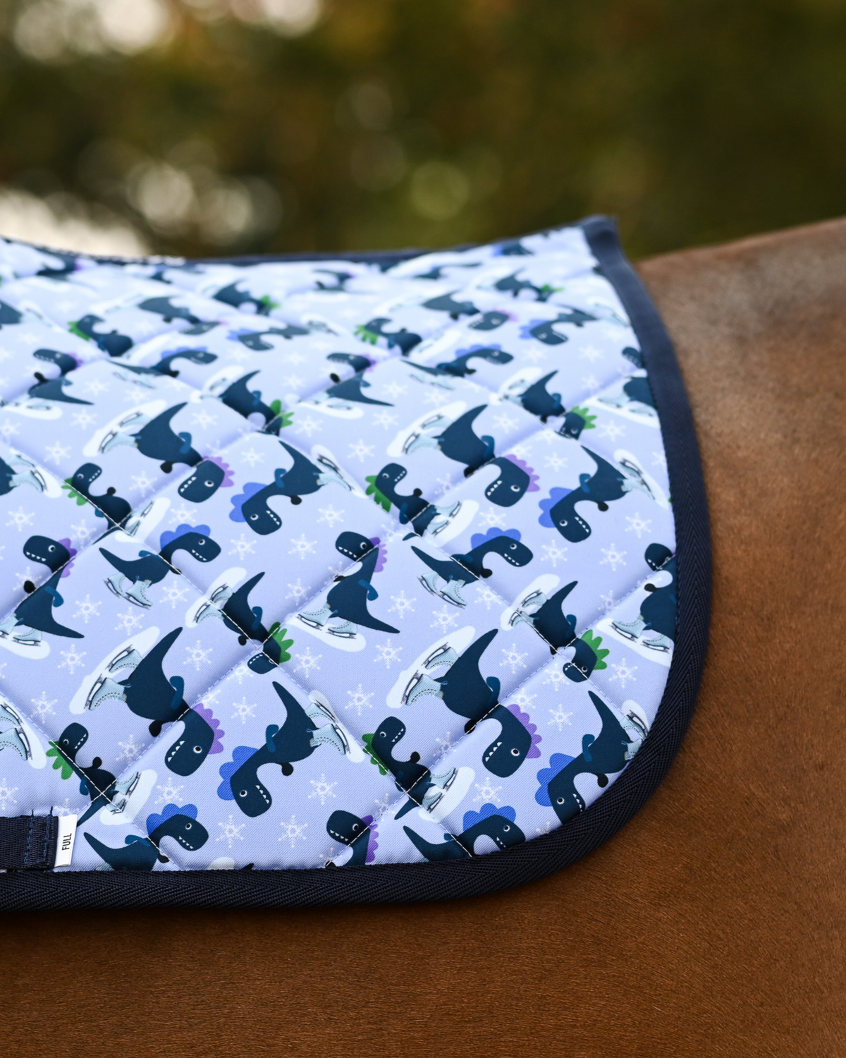 Close-up of the Dino-skate print: navy and green dinosaurs on ice skates over pale periwinkle quilting