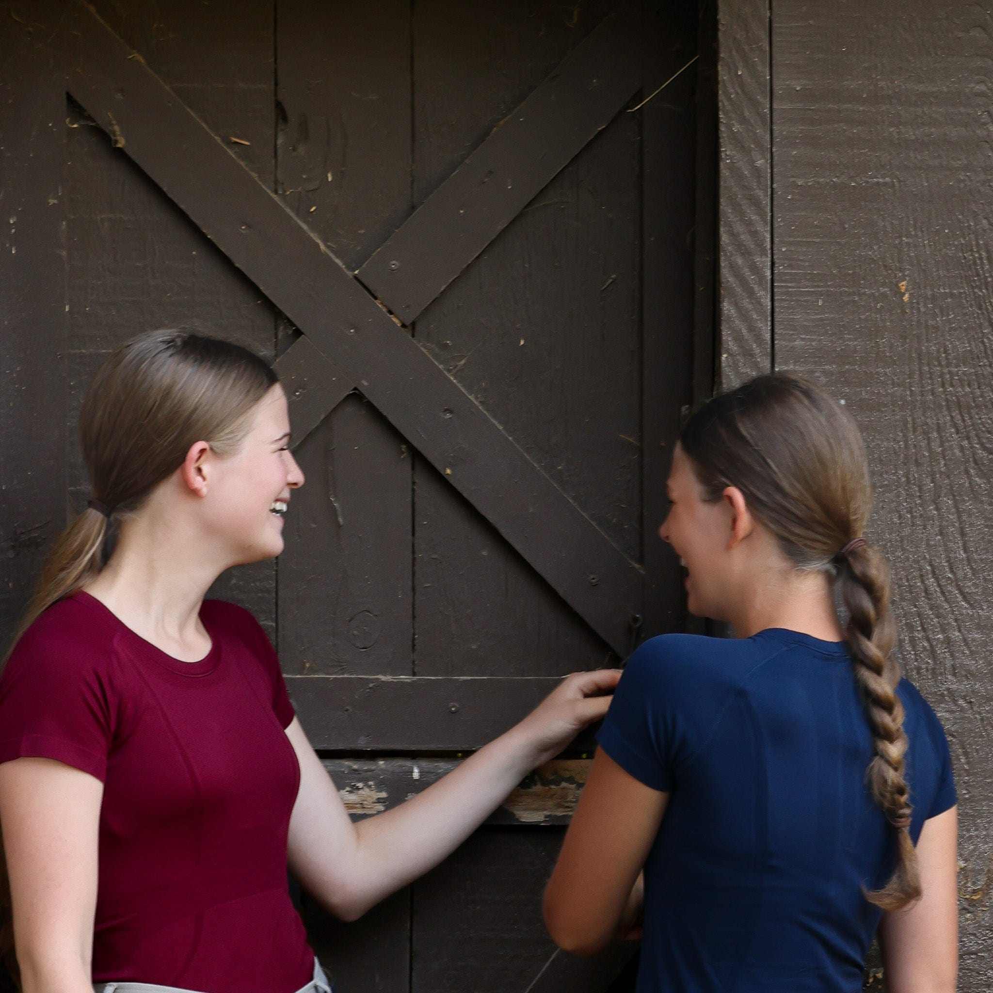 Two women wearing Equitation Tech Short Sleeve tops in navy and burgundy standing by a wooden barn door