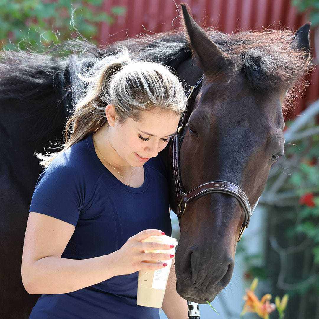 Woman wearing navy Equitation Tech Short Sleeve top standing beside a horse outdoors