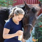 Woman wearing navy Equitation Tech Short Sleeve top standing beside a horse outdoors