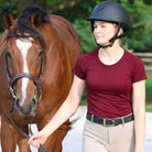 Woman wearing burgundy Equitation Tech Short Sleeve top leading horse outdoors