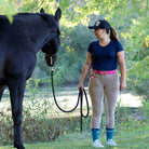 Woman wearing navy Equitation Tech Short Sleeve top with beige riding pants holding a black horse outdoors