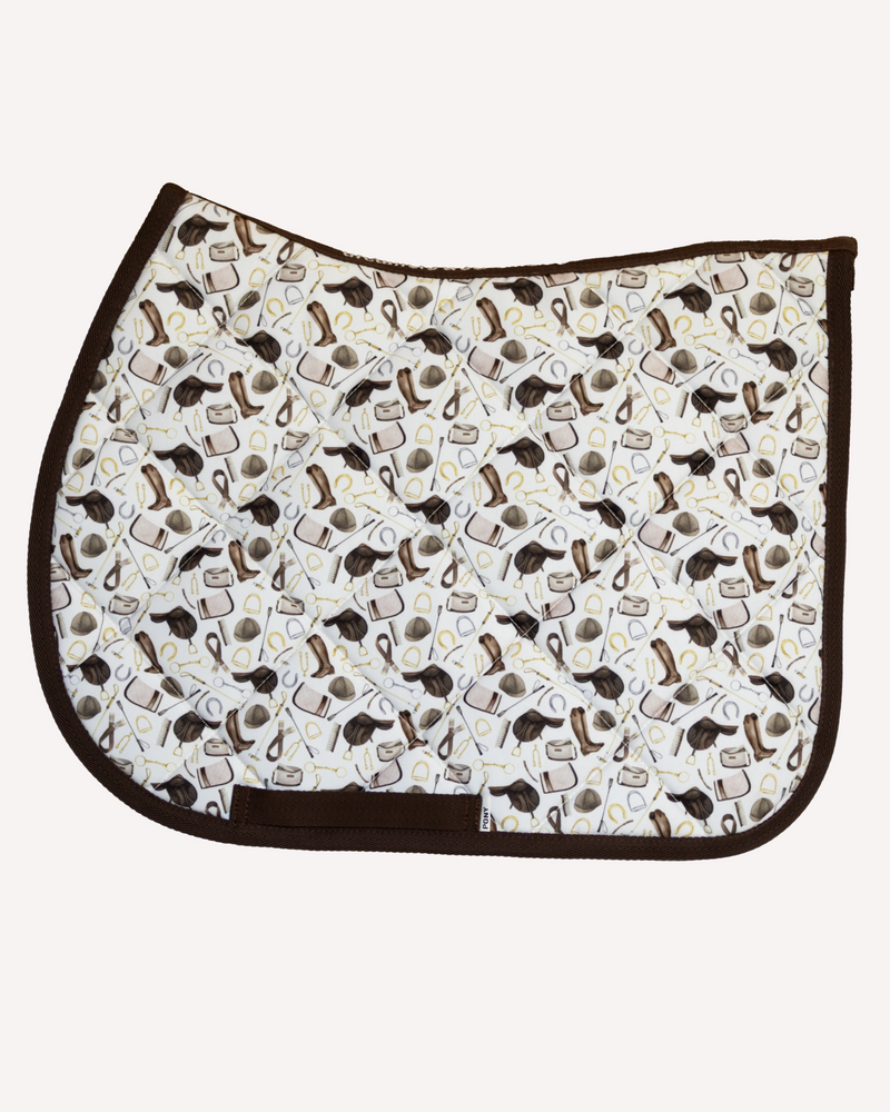 The Hunt saddle pad in cream printed with riding boots, helmets and bits, English pad shown flat by Dreamers & Schemers
