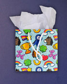 Full O' Luck small gift bag standing front-on, tissue paper above trophies, clovers and rainbows.