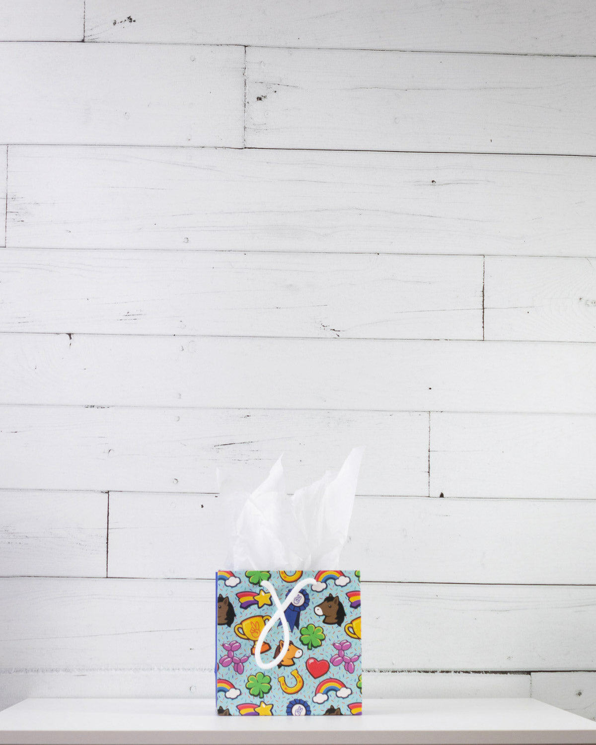 Full O' Luck small gift bag on a white shelf, aqua print of clovers, rainbows, horseshoes and hearts.