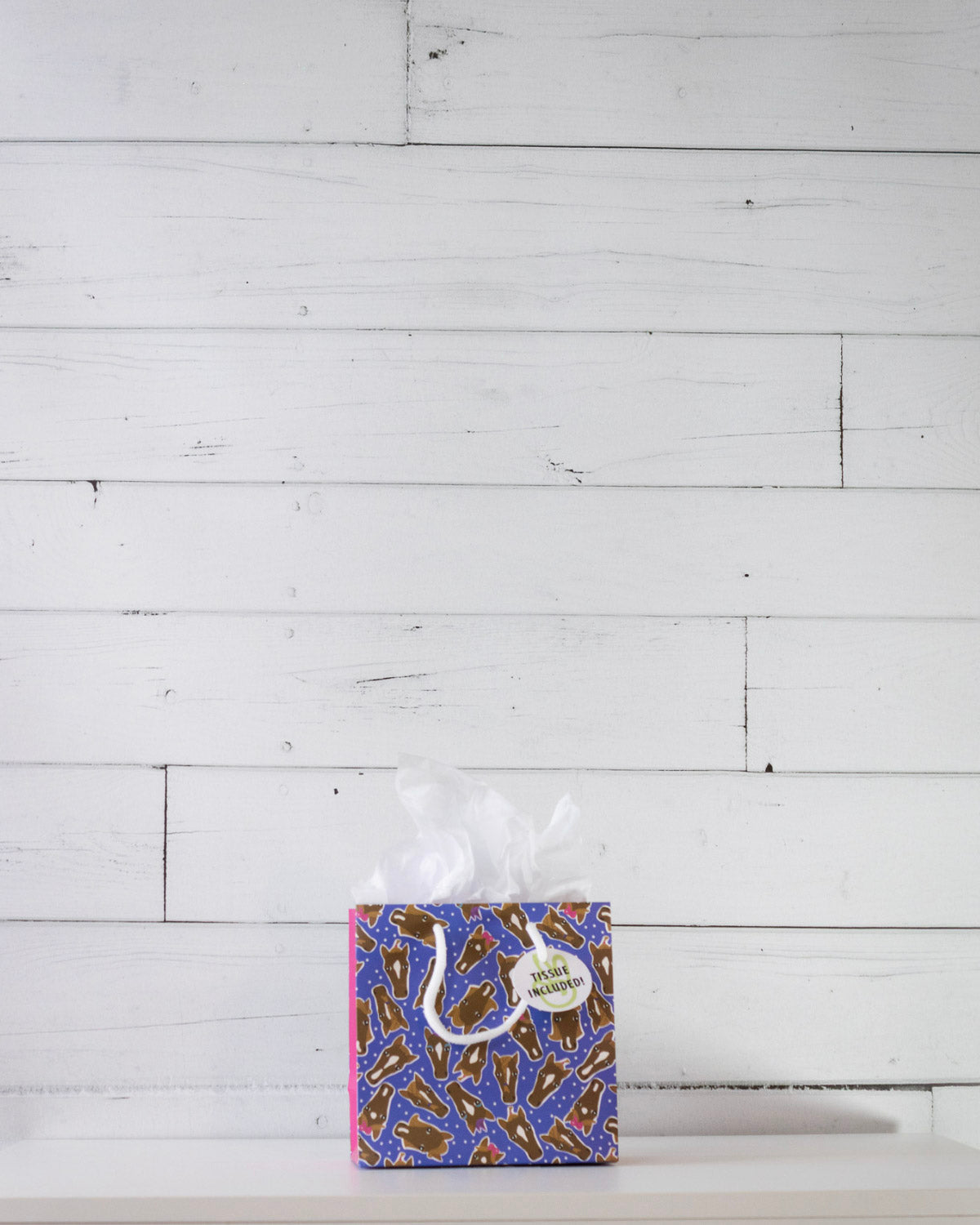 Hairy Styles small gift bag on a white shelf, square blue panel scattered with cartoon pony faces.