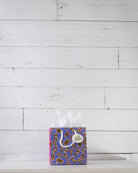 Hairy Styles small gift bag on a white shelf, square blue panel scattered with cartoon pony faces.