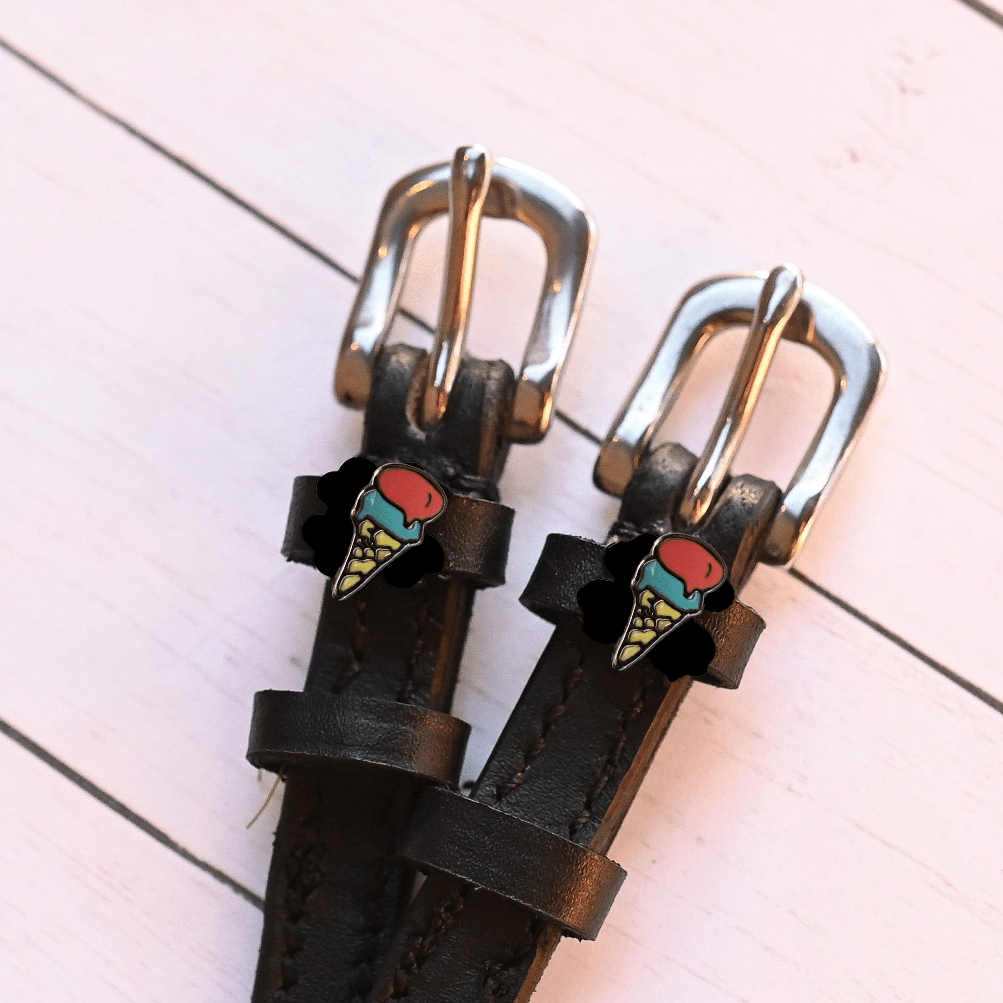 Silver buckles and ice cream cone charms of black leather spur straps on pink wood