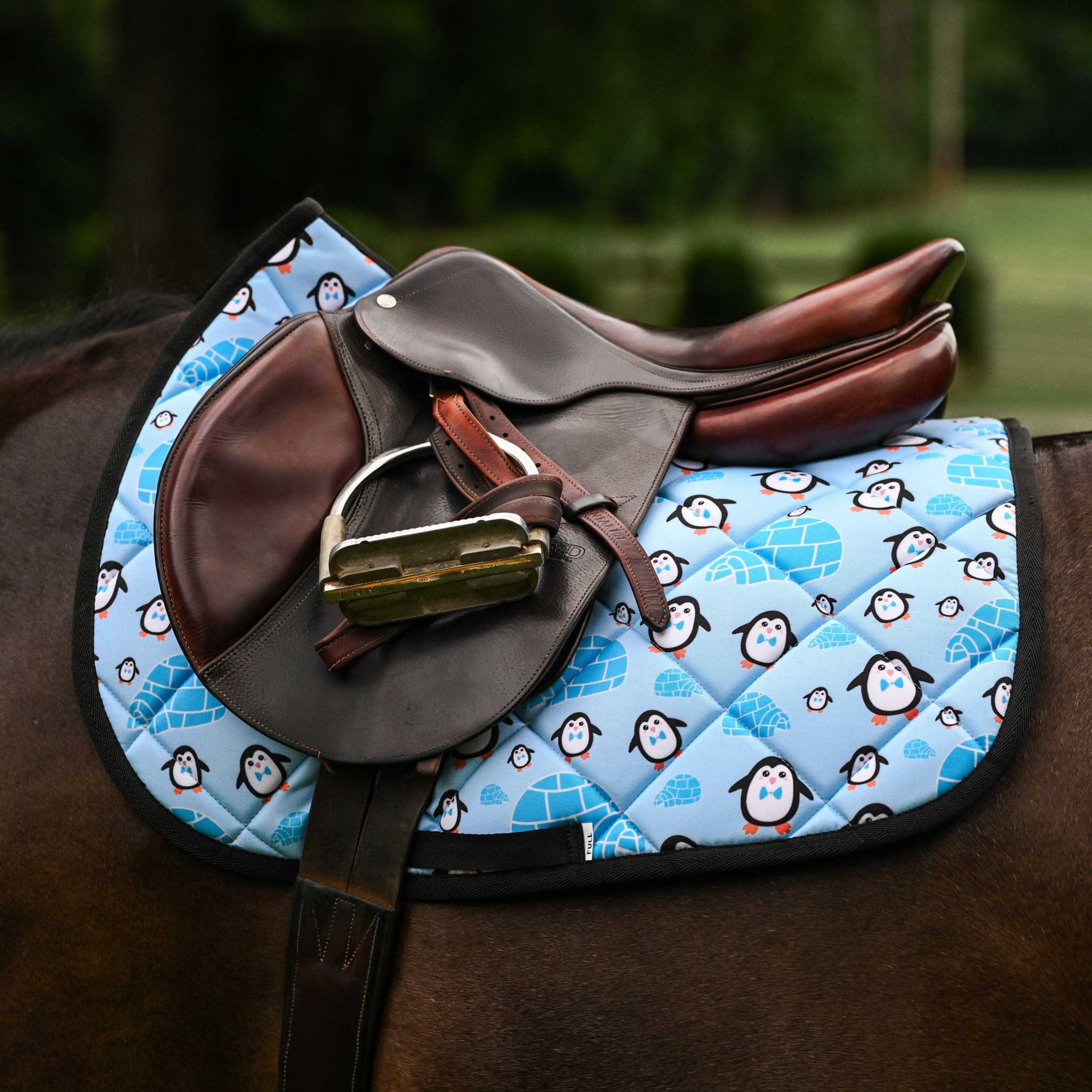 Igloo Crew Saddle Pad with penguin and igloo pattern under brown leather saddle on horse