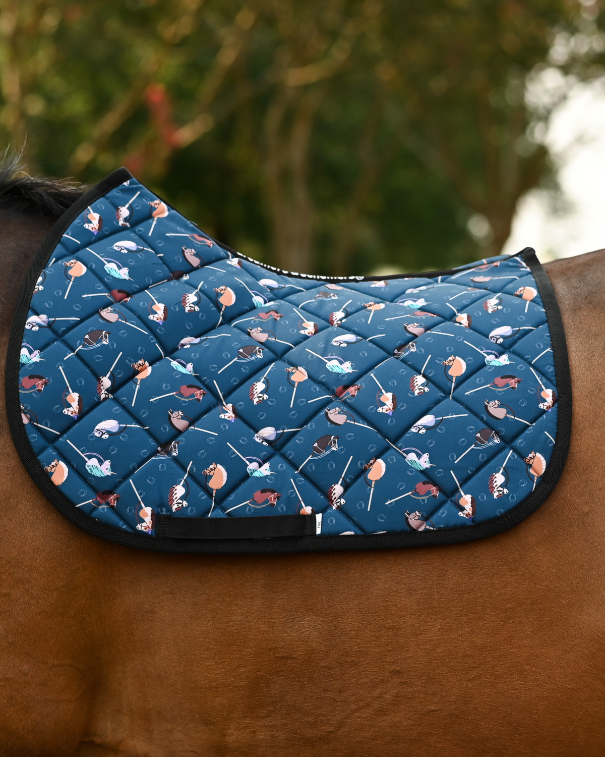 It's Not a Hobby saddle pad in dark teal, printed with stick hobby horses, shown bare on a bay horse