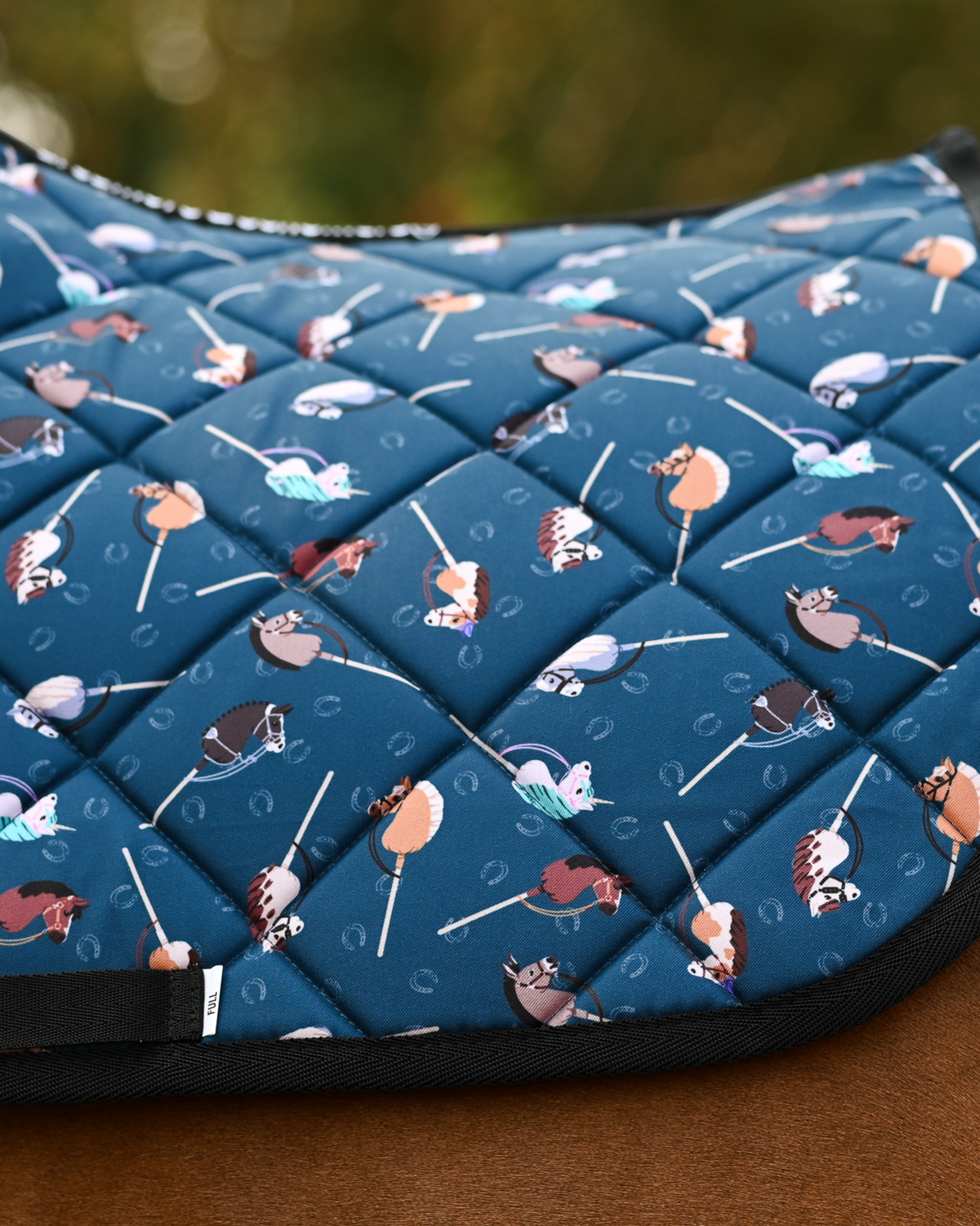 Detail of the It's Not a Hobby quilting: stick hobby horses and horseshoes on teal with black binding