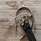 Black leather Leo Spur Straps with stainless steel buckles and custom ManeJane charms on wooden background