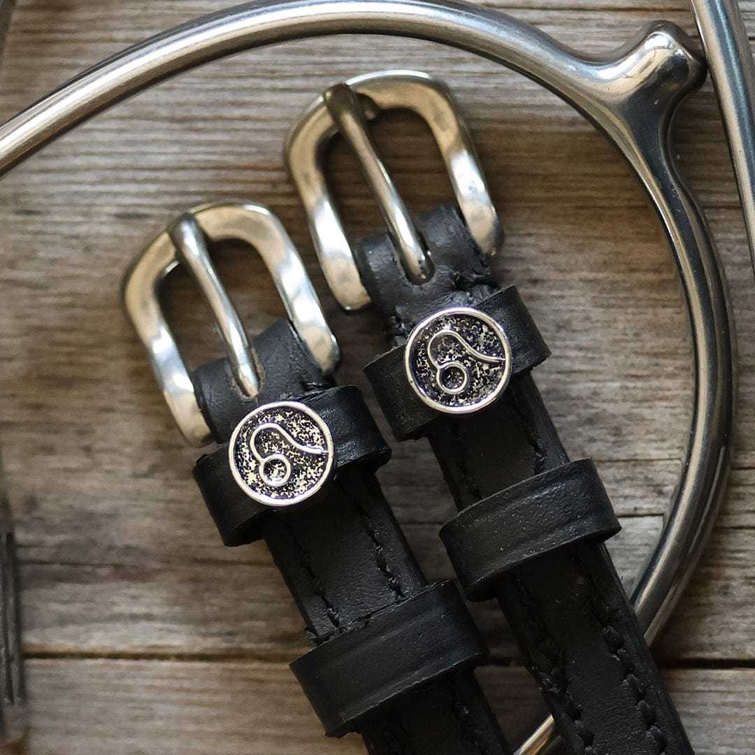 Black leather Leo Spur Straps with stainless steel buckle and custom charm on wooden background