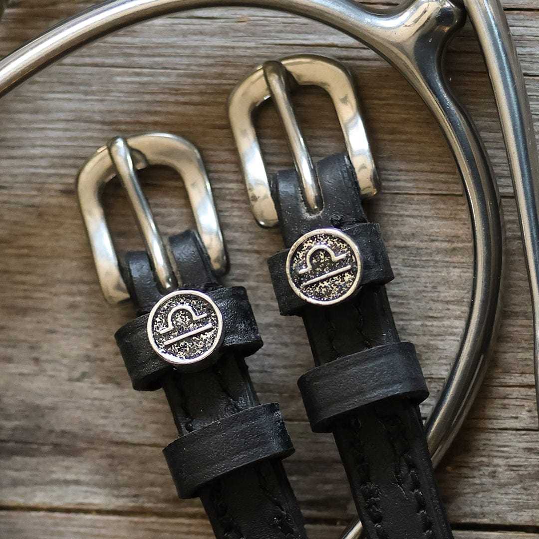 Black leather Libra Spur Straps with silver buckles and custom Libra charm on wooden background