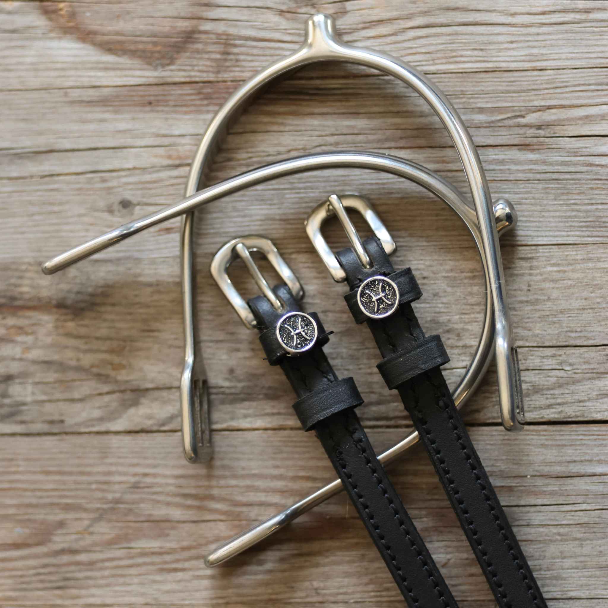 Pisces Spur Straps black leather with stainless steel buckles and custom charm on wooden background