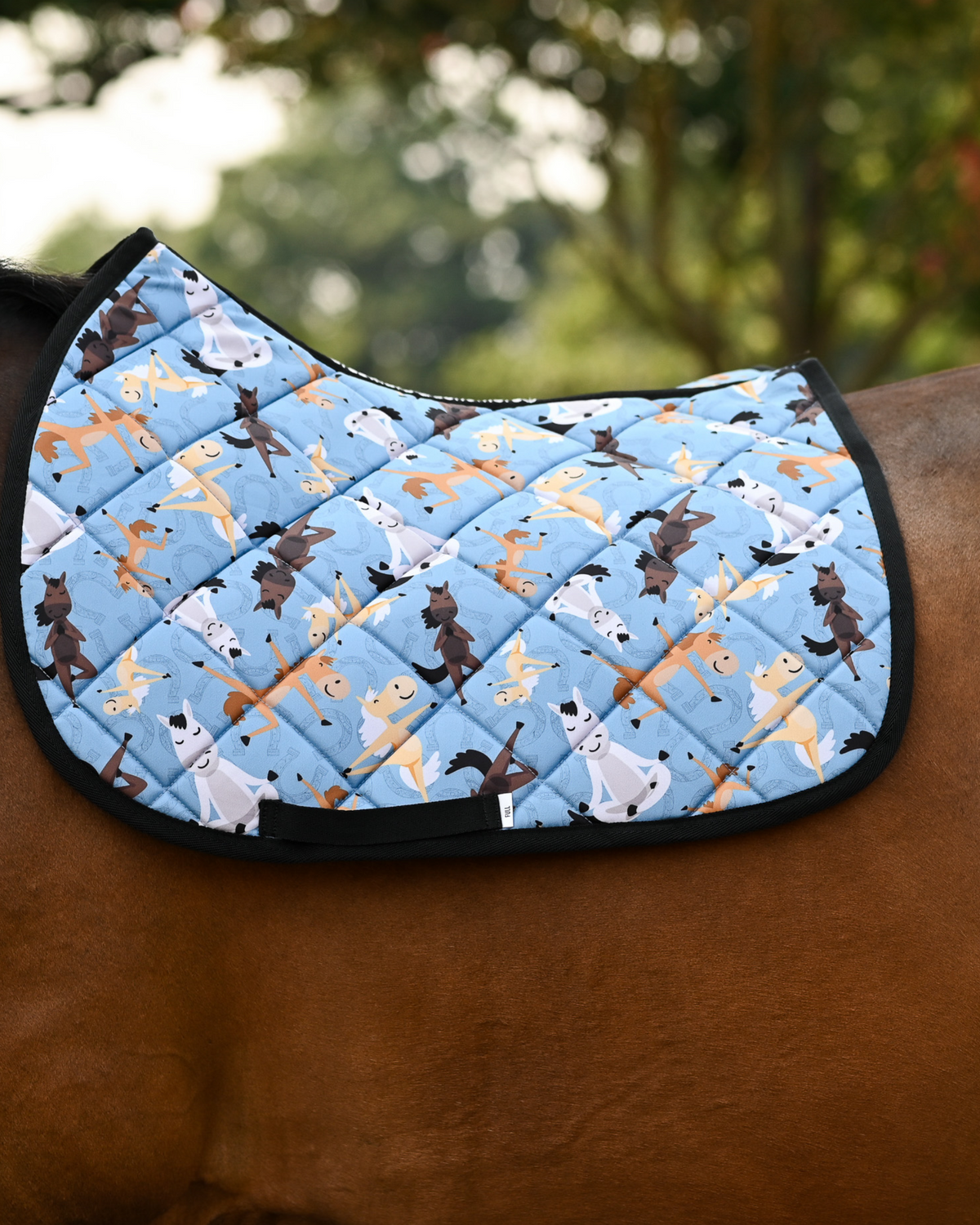 Pony Pilates saddle pad in denim blue, horses stretching in yoga poses, worn bare on a bay horse