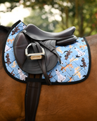 Full side view of the Pony Pilates saddle pad tacked up with a brown jump saddle against green trees