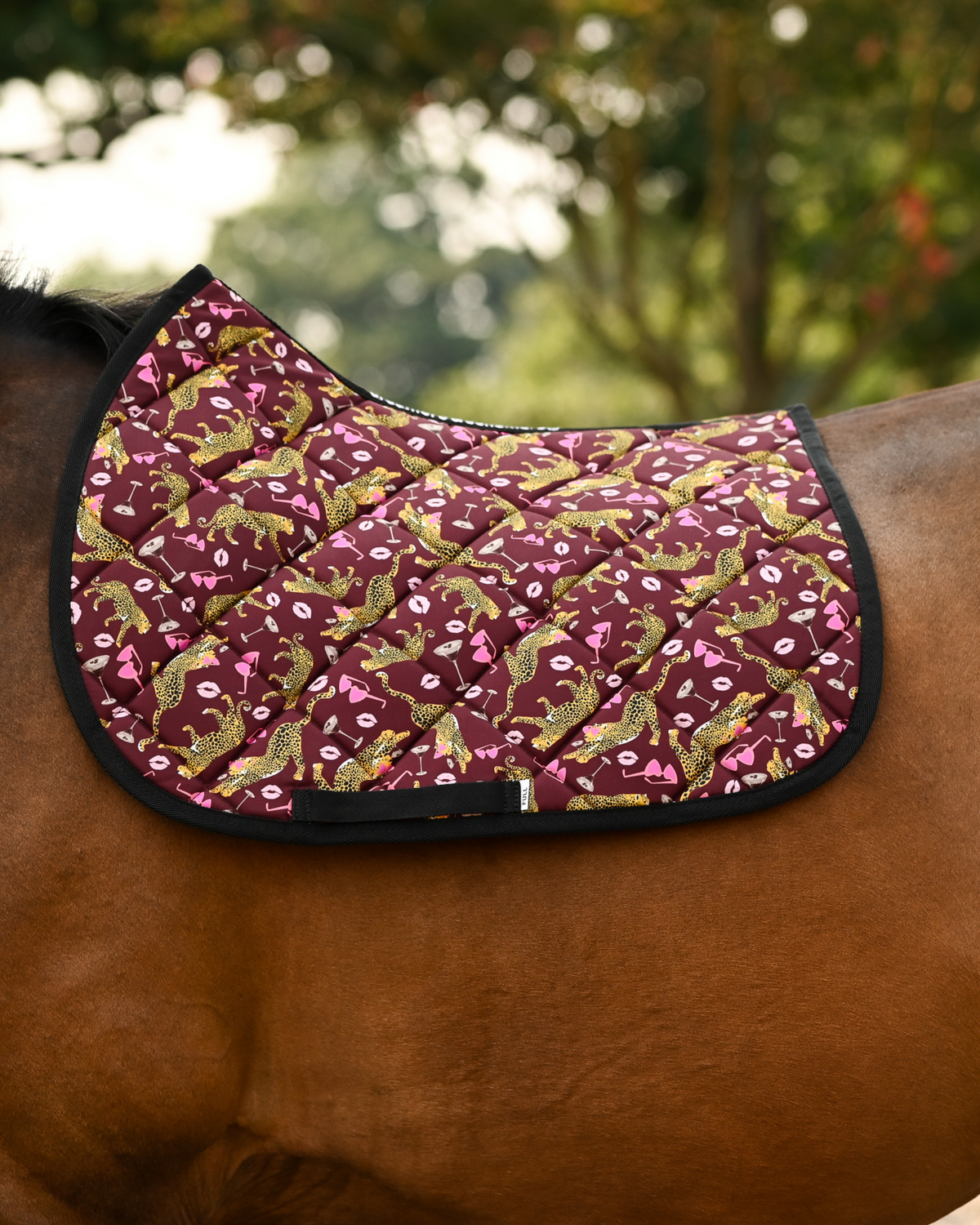 Ready to Play saddle pad in burgundy with gold leopards and pink lips, shown without a saddle