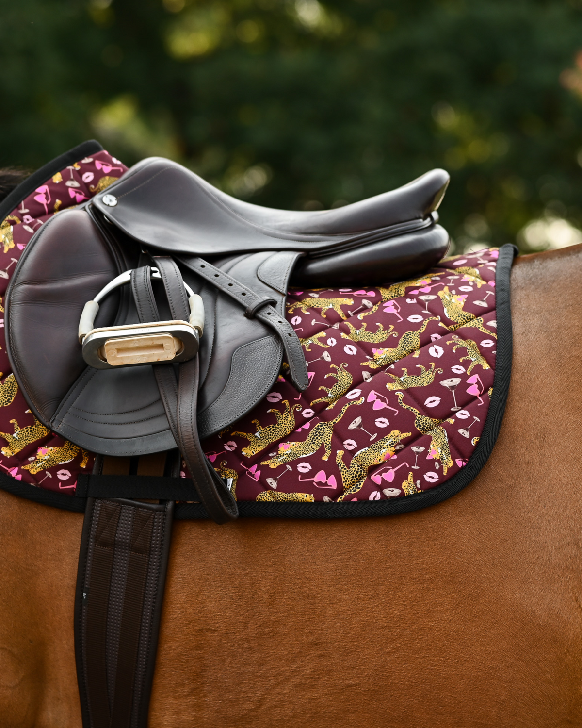 Burgundy Ready to Play pad under a brown close-contact saddle and girth on a bay horse outdoors