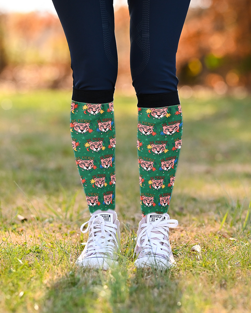 Be Brave riding boot socks worn over navy breeches with white sneakers, green tiger print showing at the calf