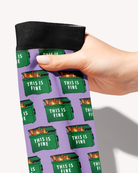 Close-up of the Dumpster Fire boot sock held by its black cuff, flaming green dumpsters reading This Is Fine on lilac