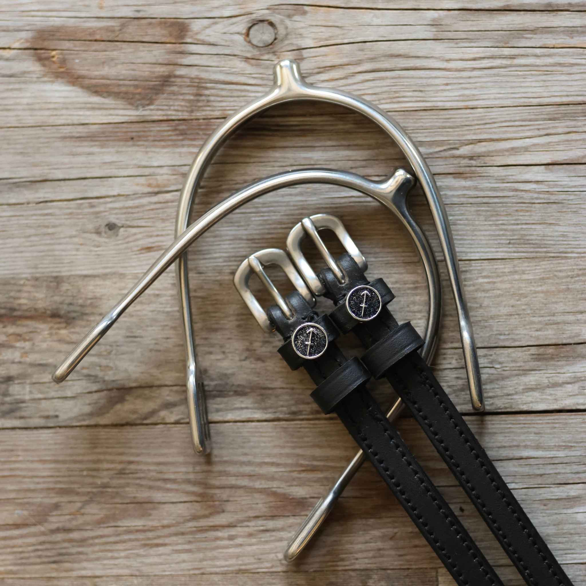 Black leather Sagittarius Spur Straps with stainless steel buckles and custom charms on wooden background