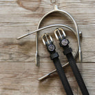 Black leather Scorpio Spur Straps with stainless steel buckles and custom charm on wood background