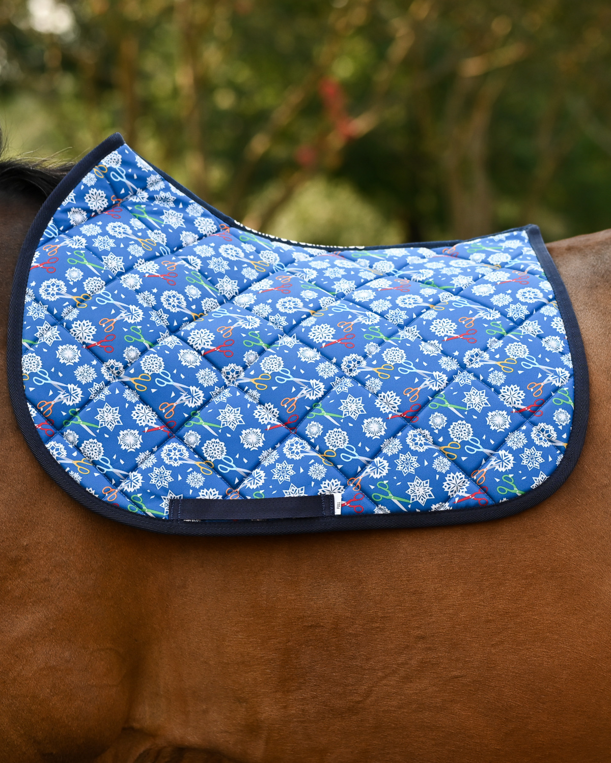 Shear Magic saddle pad in royal blue with white paper-cut snowflakes, shown bare on a bay horse
