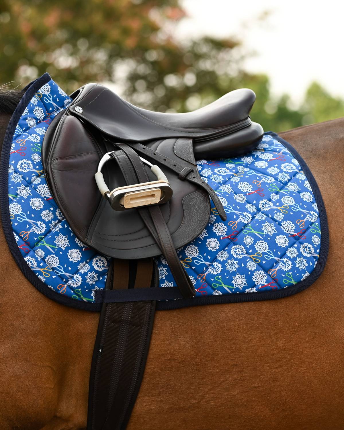 Royal blue Shear Magic pad under a brown close-contact saddle, snowflakes and craft scissors on show