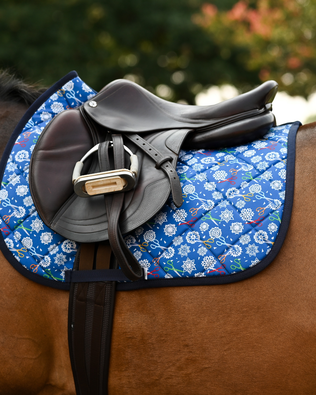 Side view of the Shear Magic saddle pad beneath a brown jumping saddle and stirrup on a bay horse