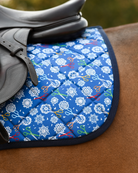 Angled view of the royal blue Shear Magic pad, part-covered by a dark brown saddle flap and girth