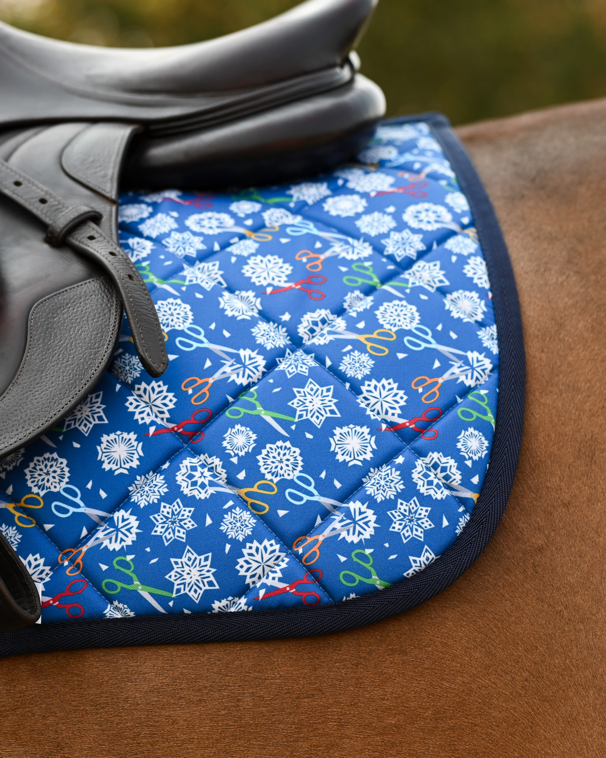 Angled view of the royal blue Shear Magic pad, part-covered by a dark brown saddle flap and girth