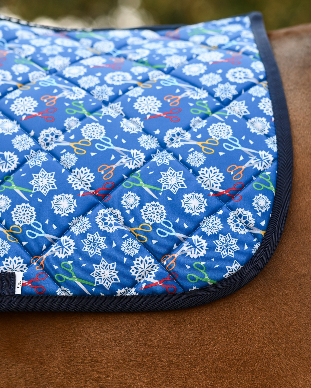 Close crop of the Shear Magic print — white snowflakes and coloured scissors on royal blue quilting
