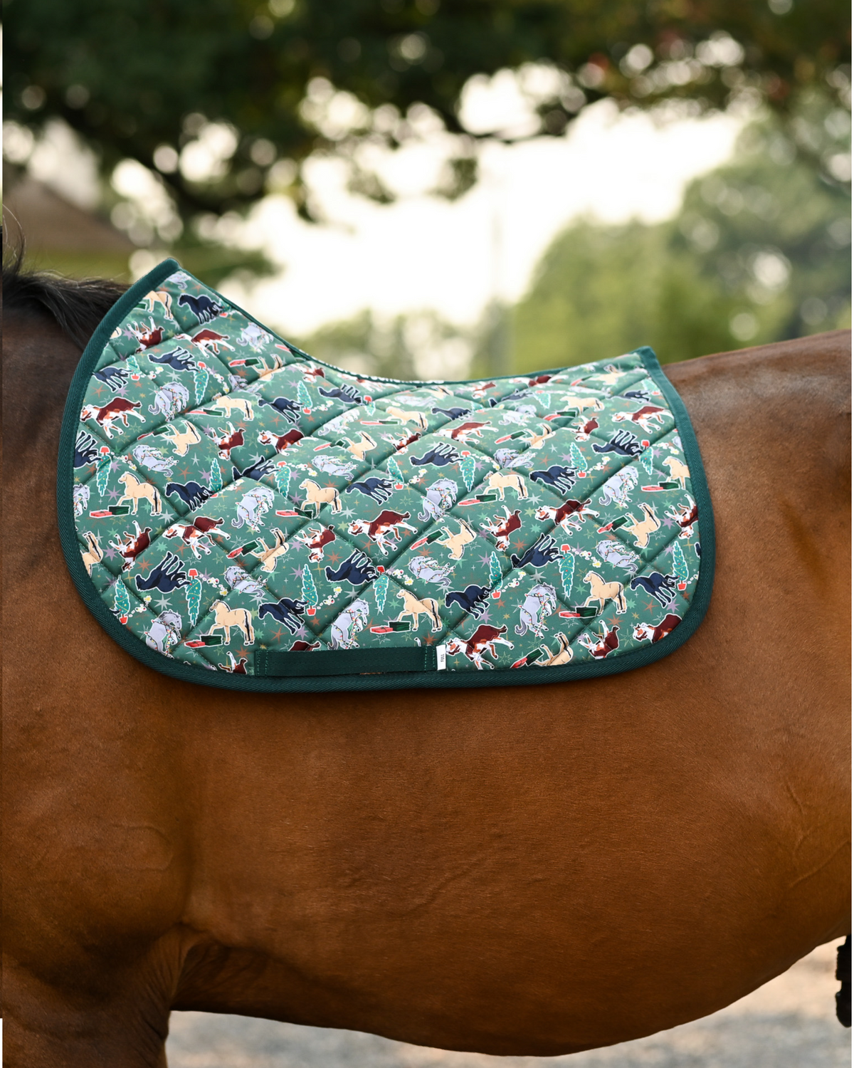 The Naughty List saddle pad in green, horses tangled in Christmas lights, worn without a saddle