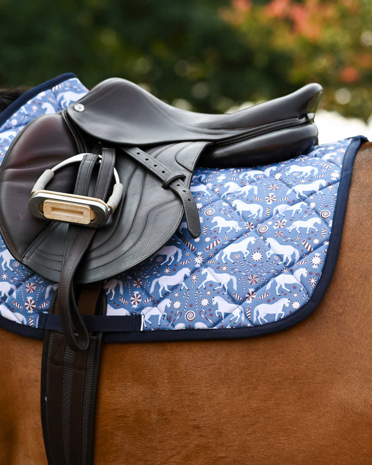 Peppermint Ponies holiday pad under a brown jumping saddle on a chestnut horse, navy binding